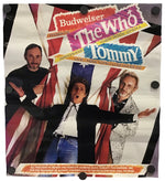A vintage Budweiser 'The Who Tommy' concert poster mounted on a white wall with black binder clips. The poster features the band members in front of a stylized Union Jack background with bold multicolored text.