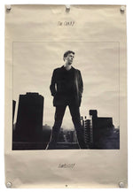 A vintage-style poster print of singer Tim Curry standing on a rooftop, displayed with binder clips on a light beige sheet of paper against a white background.