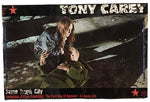 A rectangular printed cover or poster featuring the text 'TONY CAREY' at the top and 'Some Tough City' at the bottom, with a dark scene showing a woman kneeling beside a person on the ground. The item is photographed against a plain white background.