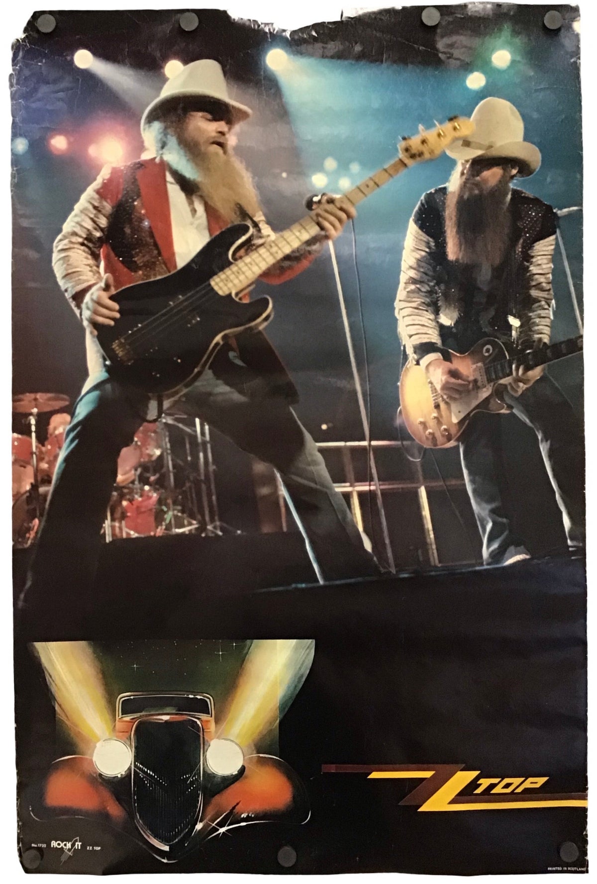 A vertical printed poster or canvas featuring two male musicians performing on stage, with stage lights and a hot rod graphic at the bottom. The print is photographed against a plain white background.