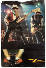 A vertical printed poster or canvas featuring two male musicians performing on stage, with stage lights and a hot rod graphic at the bottom. The print is photographed against a plain white background.