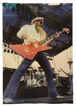 A rectangular printed poster or photo print featuring a live concert scene of a bearded male musician playing a red electric guitar on stage, shown against a plain white background.